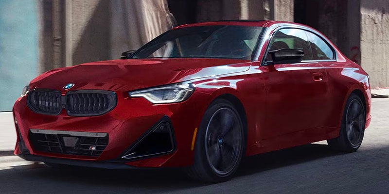 Dark green BMW luxury sedan driving on a winding road through a scenic hillside landscape