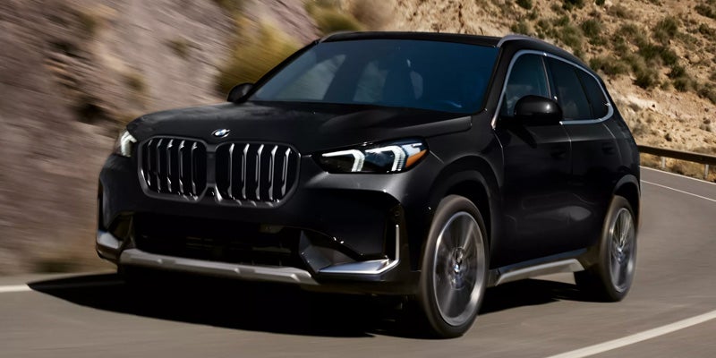 Black BMW SUV parked in front of a modern building with large overhangs and a tree-lined driveway