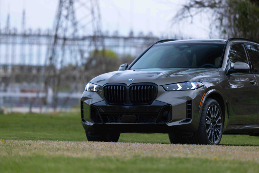 Front view of a grey 2026 BMW X5 luxury SUV parked in a grassy field